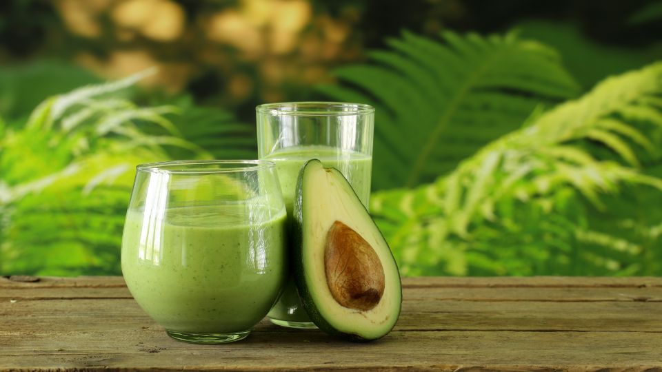 Avocado-Sorten, Pflanztipps und Krankheiten Ein frischer Avocado-Smoothie in Gläsern mit einer halbierten Avocado auf einem Holztisch.