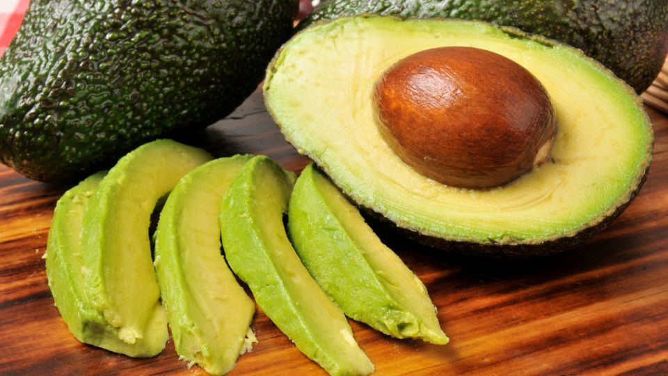 Avocado-Sorten, Pflanztipps und Krankheiten Eine halbierte Avocado mit einem großen Kern und geschnittenen Scheiben auf einem Holzbrett.