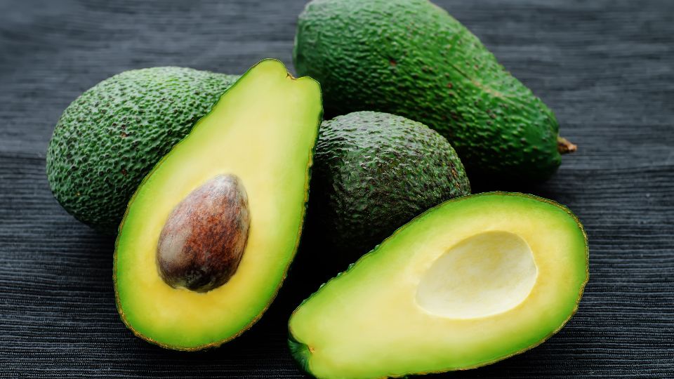 Reife Avocados, eine aufgeschnittene Frucht zeigt das grüne Fruchtfleisch und den Kern.