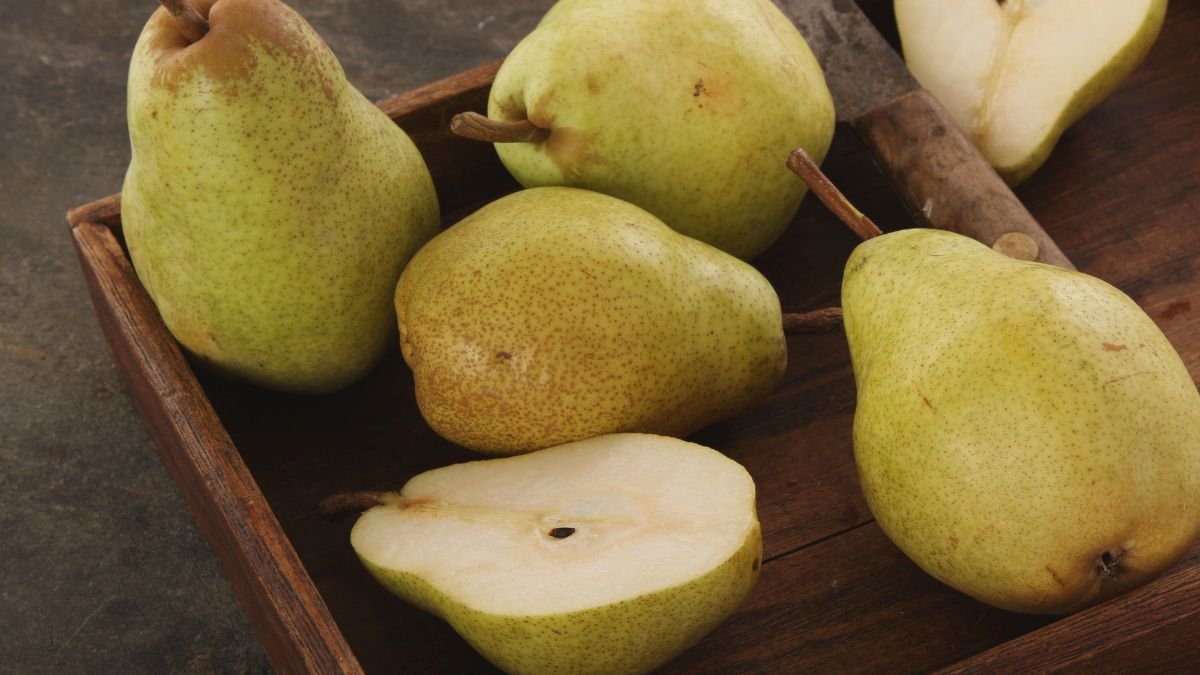Fünf reife Birnen, eine aufgeschnitten, liegen auf einem Holzbrett.