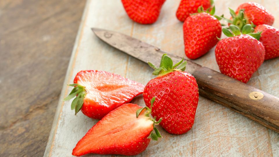 Frische Erdbeeren und ein Messer auf einem Holzbrett.