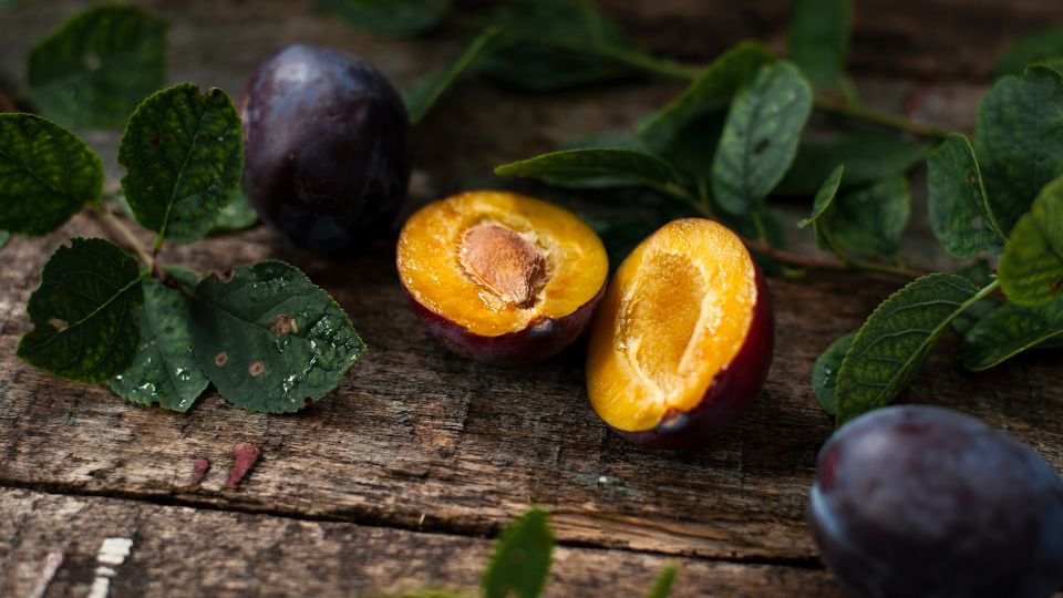 Frische Pflaumen und Blätter auf einem rustikalen Holztisch.