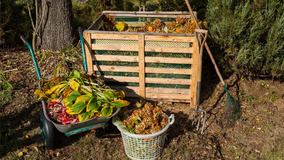 Ein Komposthaufen aus Gartenabfällen, umgeben von Werkzeugen und Pflanzenresten.
