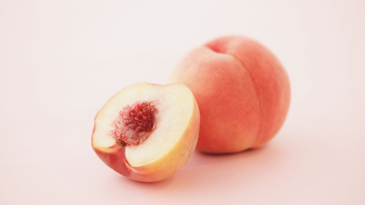 Ein reifer Pfirsich und eine halbierte Frucht mit saftigem Fruchtfleisch.