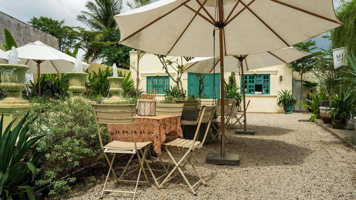 Ein Kiesgarten mit einem Tisch und Stühlen unter Sonnenschirmen, umgeben von Pflanzen.