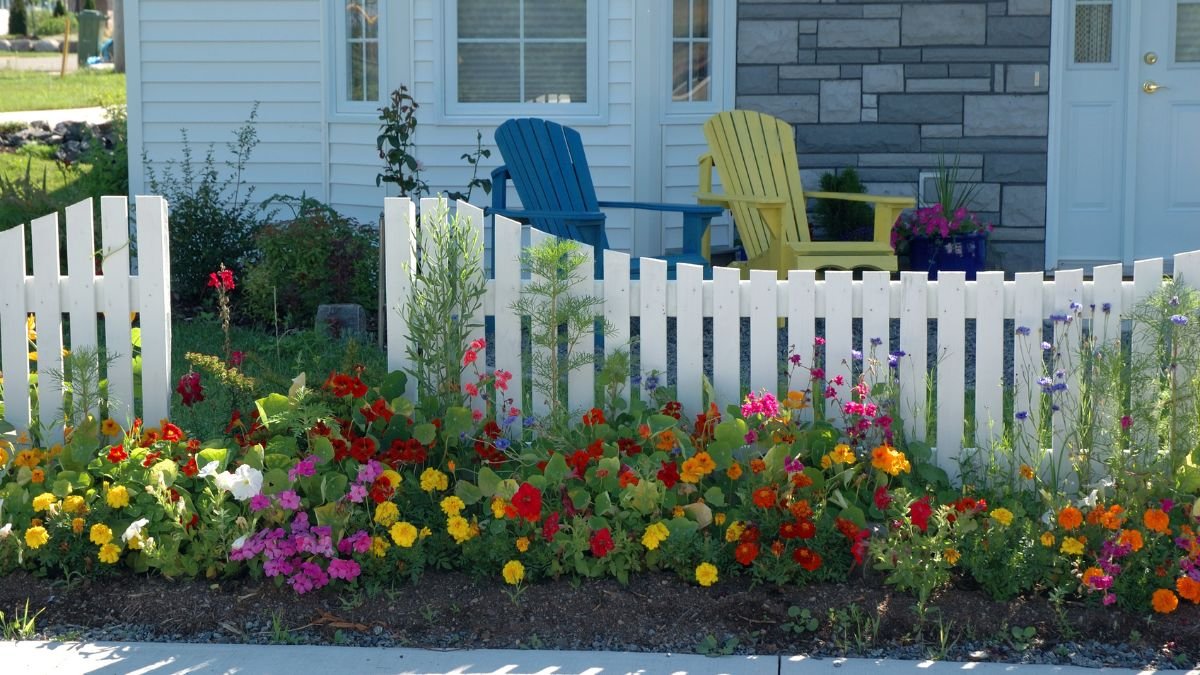 Ein weißer Gartenzaun umgeben von bunten Blumen im Landhausstil.