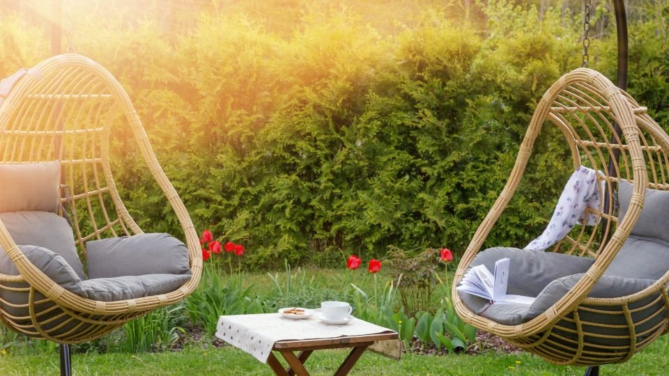 Zwei schwingende Korbsessel im Garten mit einer Tasse und einem Buch auf einem Tisch.