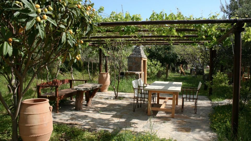 Ein mediterraner Garten mit einer Holzterrasse, Tisch und Stühlen, umgeben von Pflanzen.