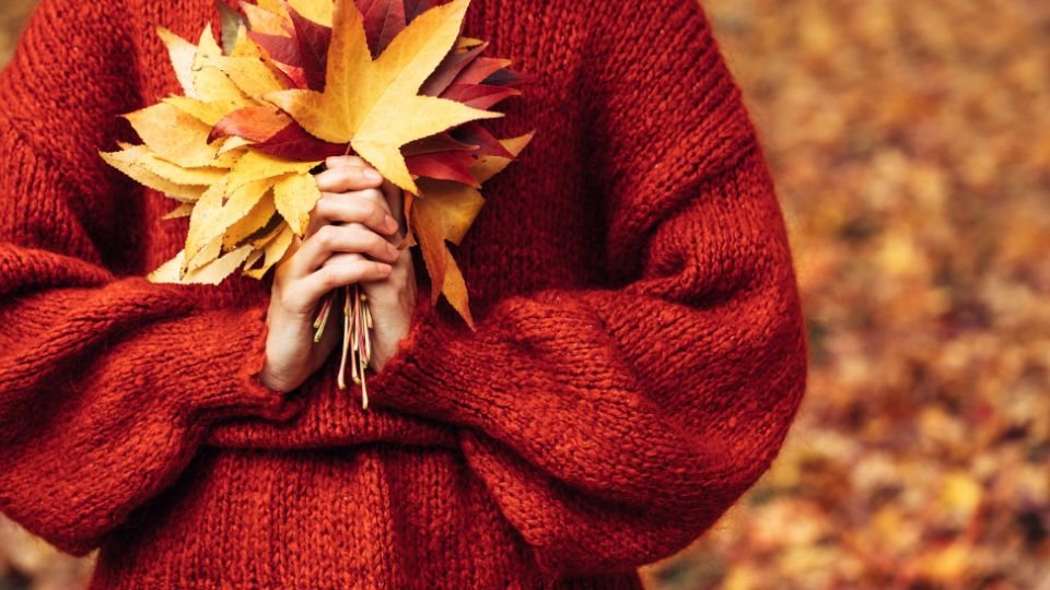Eine Person hält einen Strauß aus bunten Herbstblättern in den Händen.