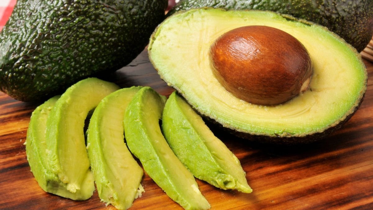 Eine aufgeschnittene Avocado mit grünen Scheiben auf einem Holzbrett.