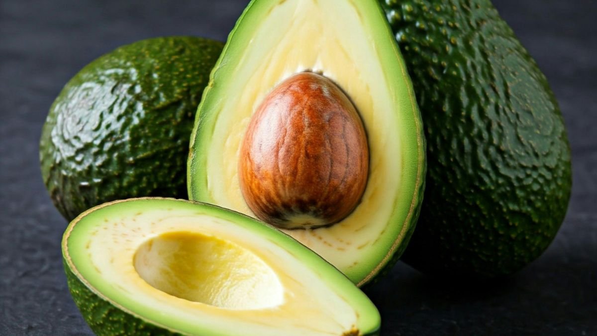 Eine halbierte Avocado mit einem großen Kern, umgeben von ganzen Avocados.