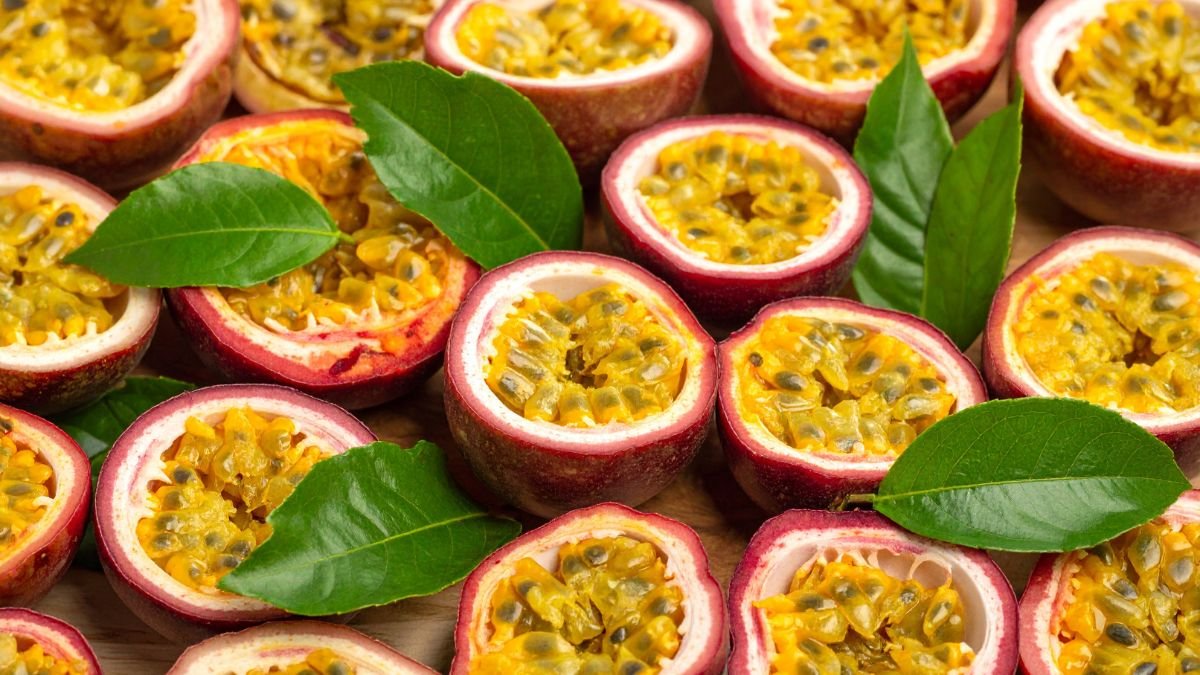 Aufgeschnittene Passionsfrüchte mit leuchtend gelbem Fruchtfleisch und grünen Blättern.