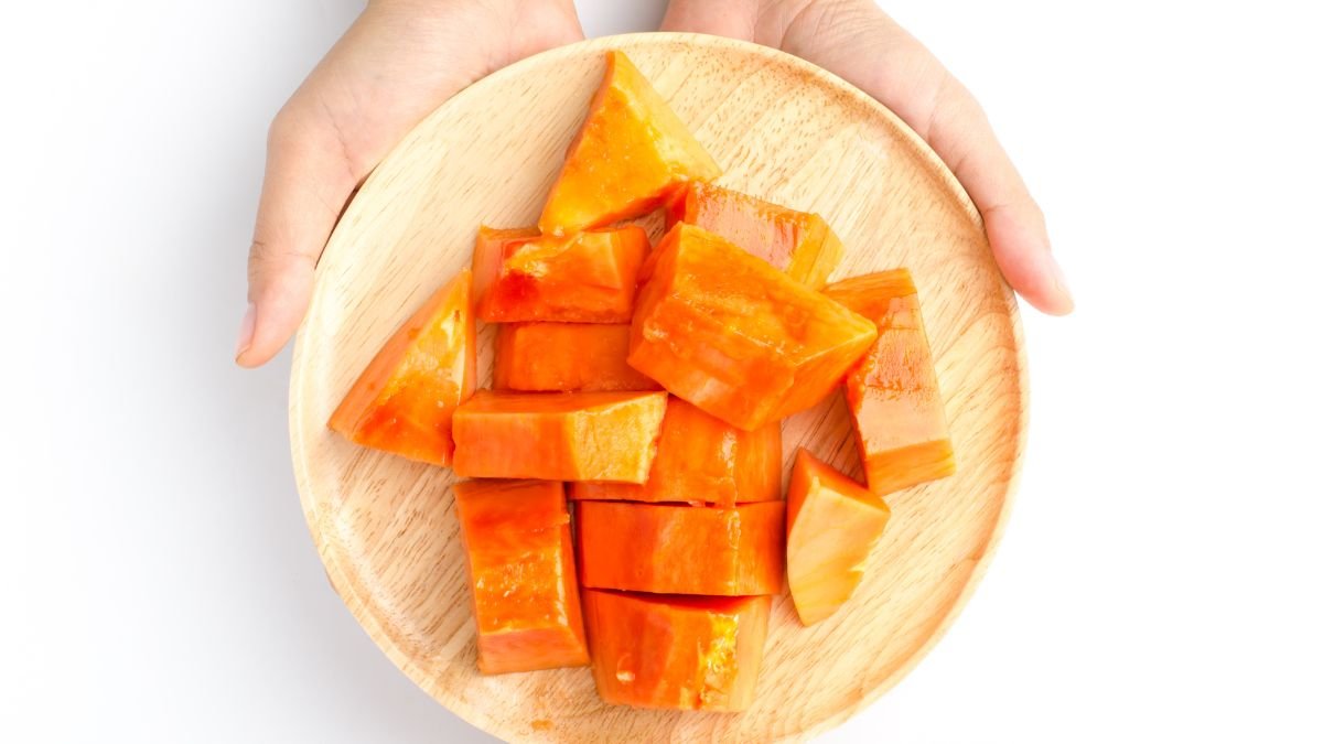Eine Hand hält einen Holzbrett mit frisch geschnittenen Papayastücken.