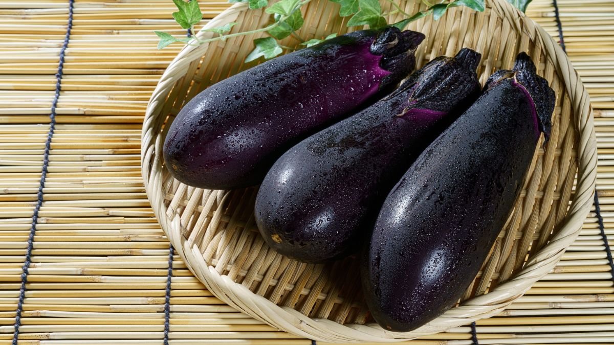 Drei frische, glänzende Auberginen auf einem Korb aus Naturmaterialien.